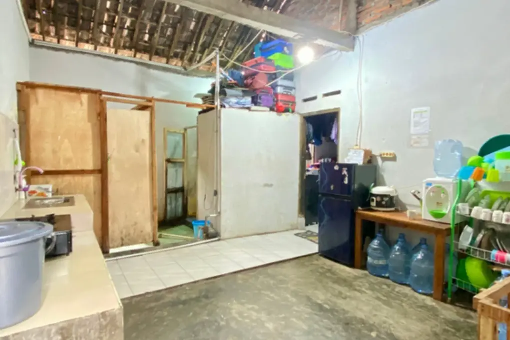 Dapur kontrakan dengan rangka atap yang masih terbuka, galon air, dan rak piring